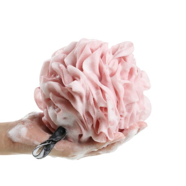 A person holding a pink Shower Bath Sponges Loofahs Ball with a pair of scissors.