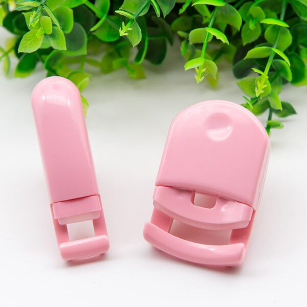 A pair of pink plastic Portable Eyelash Curlers for Women next to a plant.